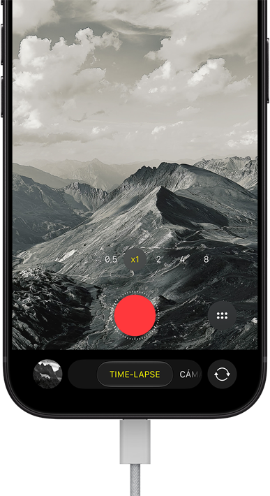 iPhone 18 Pro, parte delantera, muestra un paisaje montañoso, ventana superpuesta del modo Cámara en time-lapse, cable de corriente conectado al puerto de carga