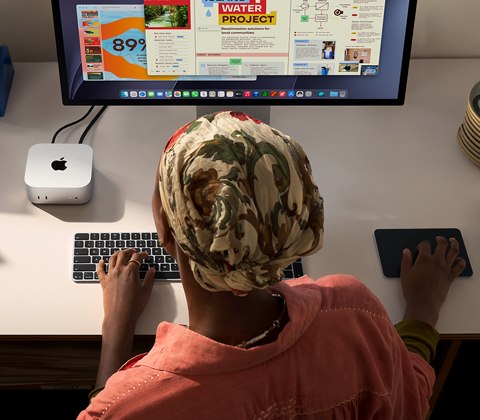 Una persona utiliza un Mac mini con Magic Keyboard, Magic Trackpad y Studio Display conectado en un escritorio
