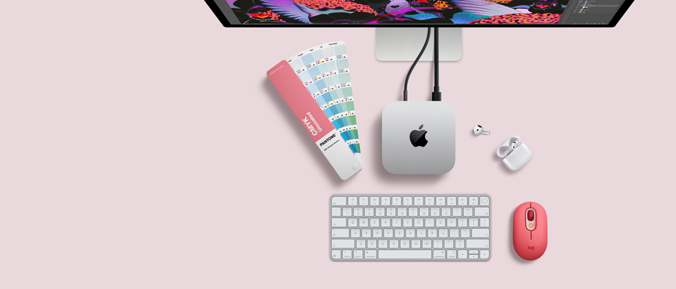 Mac mini, vista superior, muestra el aluminio en plata, las esquinas redondeadas, el logotipo negro y brillante de Apple en el centro, el cable de conexión, la parte superior del Studio Display, los AirPods 4 abiertos, las tarjetas de colores Pantone y el teclado y el ratón Logitech rojos