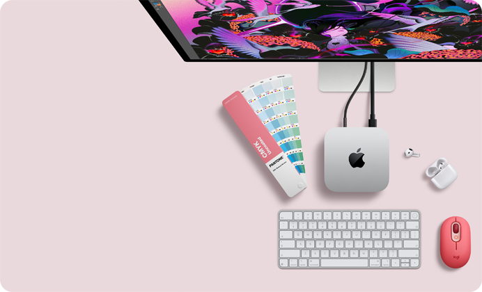 Mac mini, vista superior, muestra el aluminio en plata, las esquinas redondeadas, el logotipo negro y brillante de Apple en el centro, el cable de conexión, la parte superior del Studio Display, los AirPods 4 abiertos, las tarjetas de colores Pantone y el teclado y el ratón Logitech rojos