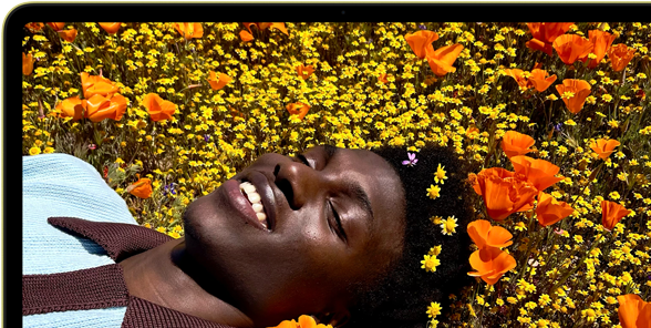 MacBook Neo, color cítrico, persona sonriente tumbada en un campo de flores en la pantalla