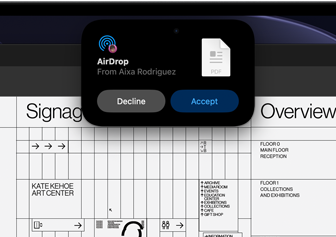 La pantalla muestra la Dynamic Island con una petición de AirDrop en una ventana pequeña sobre un archivo abierto de Adobe Acrobat