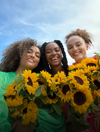 Selfie nítido y a todo color de tres personas con flores en la mano.